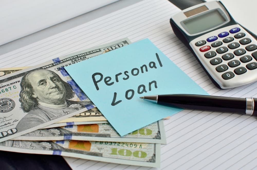 Sheet of paper with the words Personal Loan on an office desk with a calculator, notepad, pen and US dollars