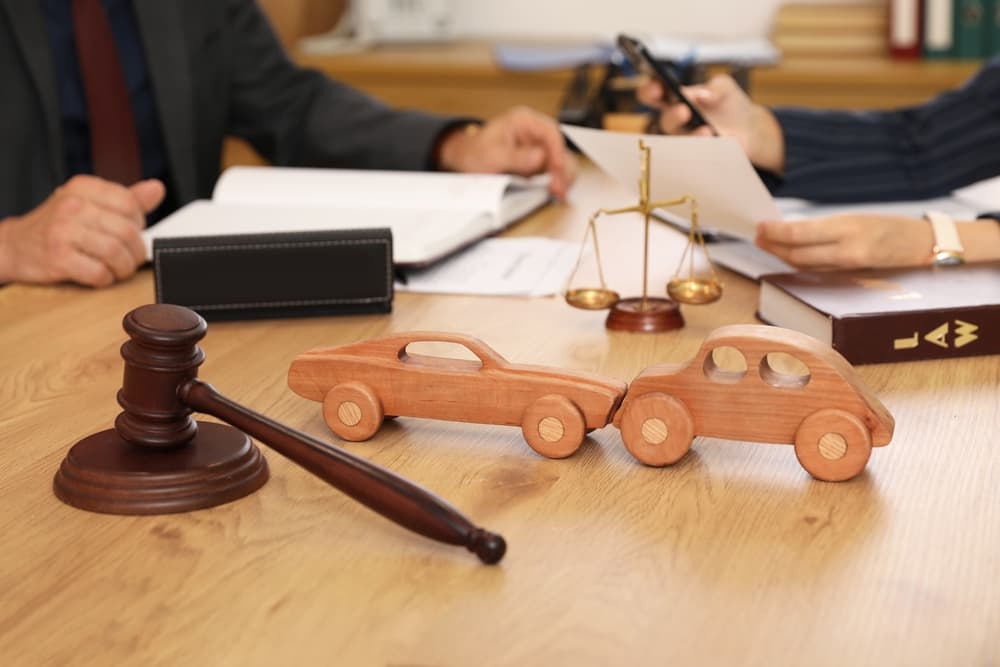 Wooden car models paired with a judge's gavel are displayed on a lawyer's desk during a meeting in an office, highlighting a legal discussion about automotive-related cases.