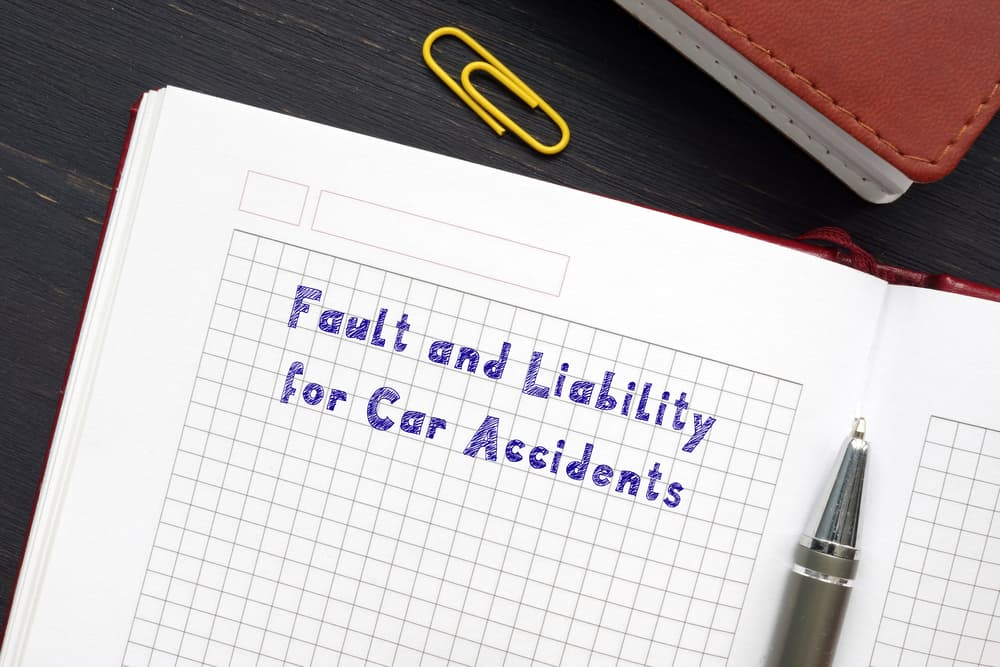 "Fault and Legal Responsibility in Car Accidents" written on the book with a pen resting beside it.