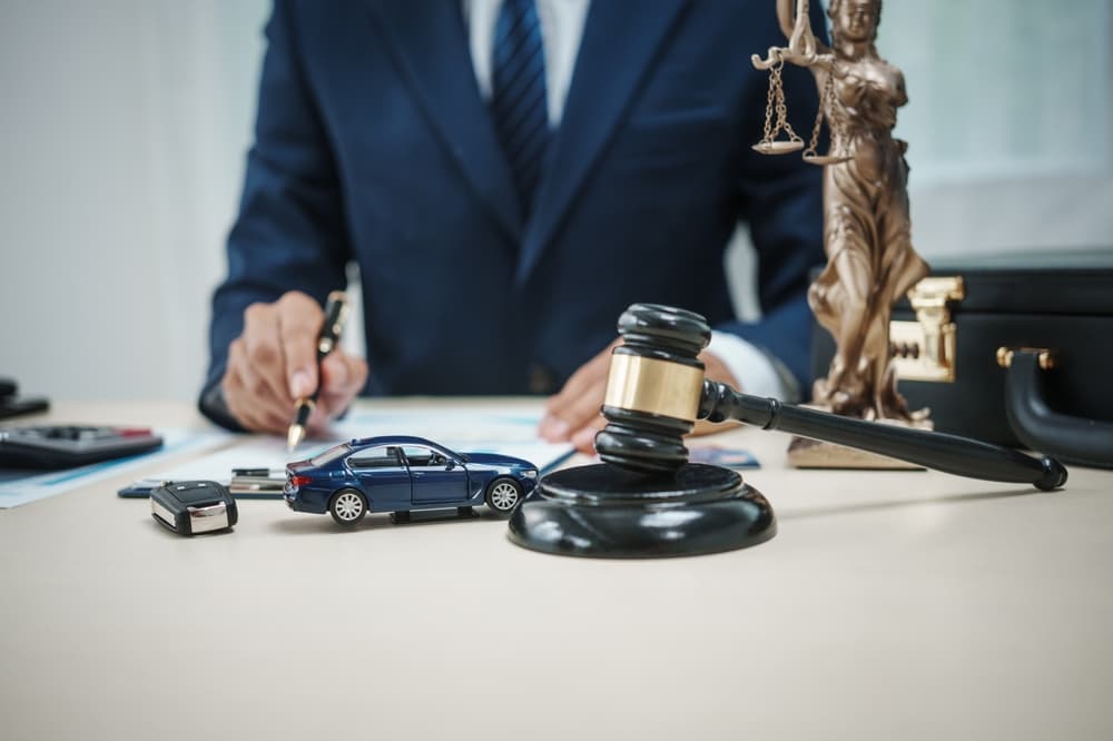 A lawyer is sitting in his office, a model of a car and a gavel on a desk, representing an accident lawsuit or insurance.